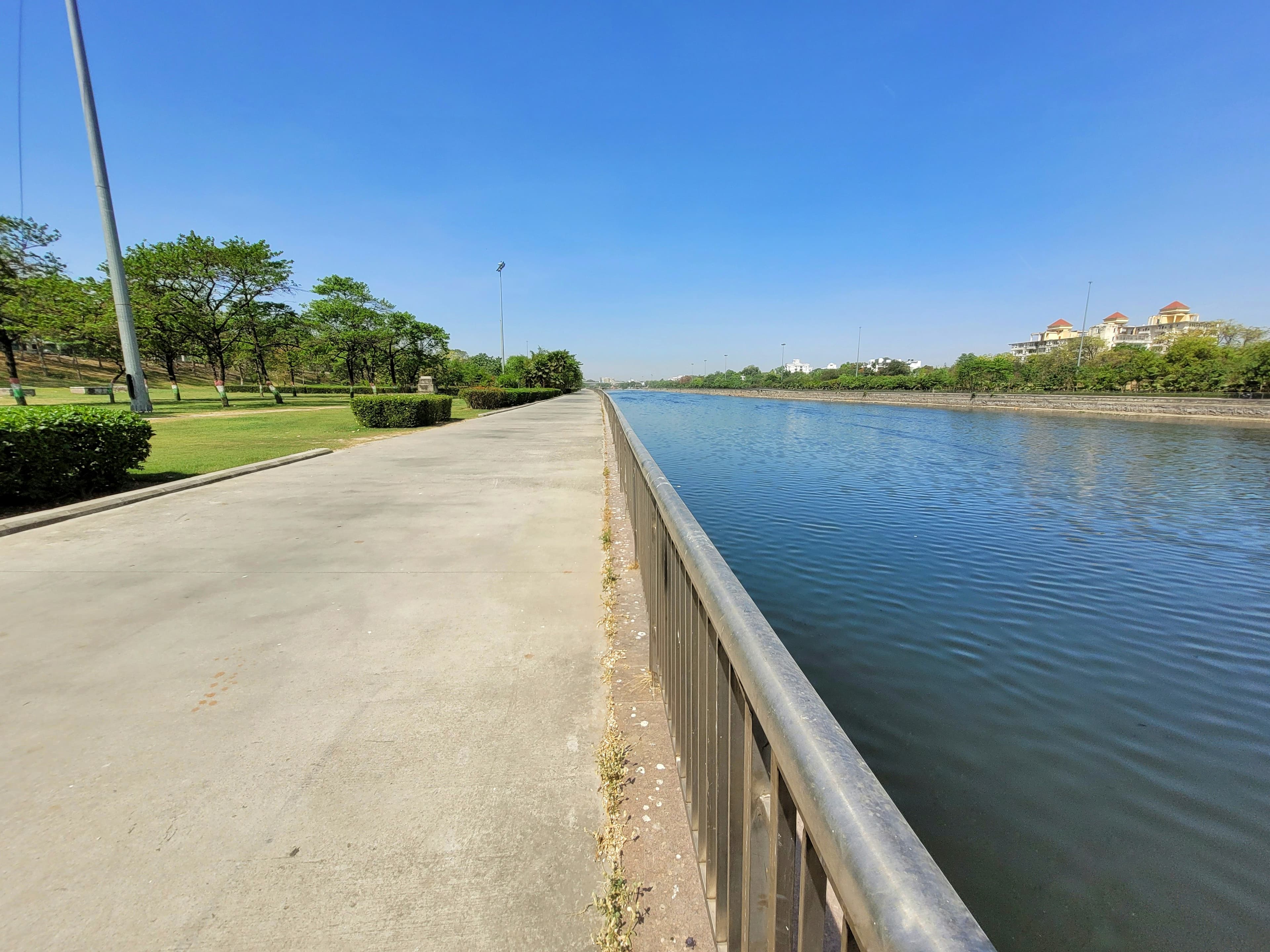 Canal promenade under clear blue sky with green trees — sustainable urban infrastructure